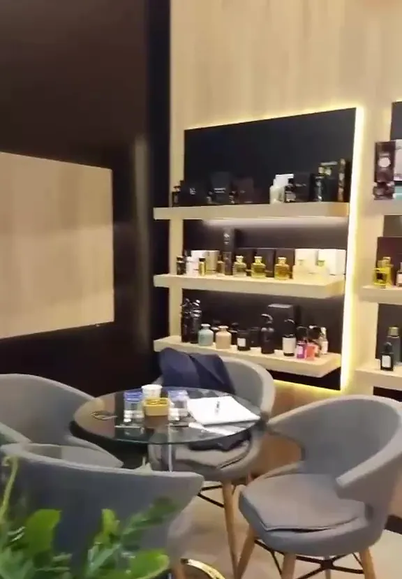 Parfüm standında ışıklı raflar ve gri koltuklu görüşme alanı
